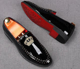 A pair of black patent leather men's loafers with a gold crown embroidery and a red bottom sole, displayed against a grey background.