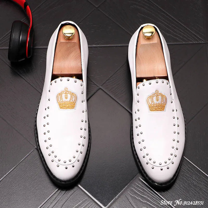 A pair of black patent leather men's loafers with a gold crown embroidery and a red bottom sole, displayed against a grey background.