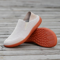 White slip-on shoes with orange soles on a wooden surface